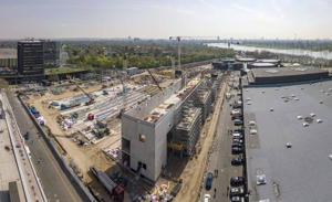 Blick über die Baustelle in Richtung Süden auf die Düsseldorfer Innenstadt im Hintergrund. Im Vordergrund zeigt sich das Rheinufer, sowie der Nordpark mit hohem Freizeitwert, der mit Zugängen zur Messe verbunden wird; eine Konstellation, die bislang einmalig in Deutschland sein dürfte.